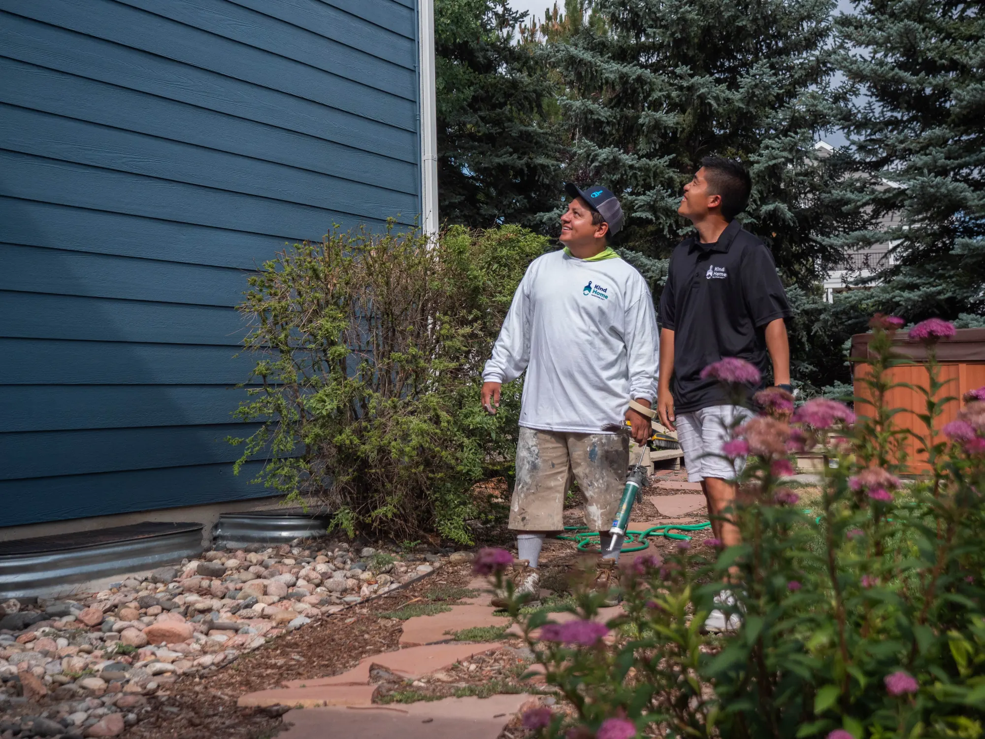 Two Kind Home painters inspecting a freshly repainted blue-gray home exterior in Denver